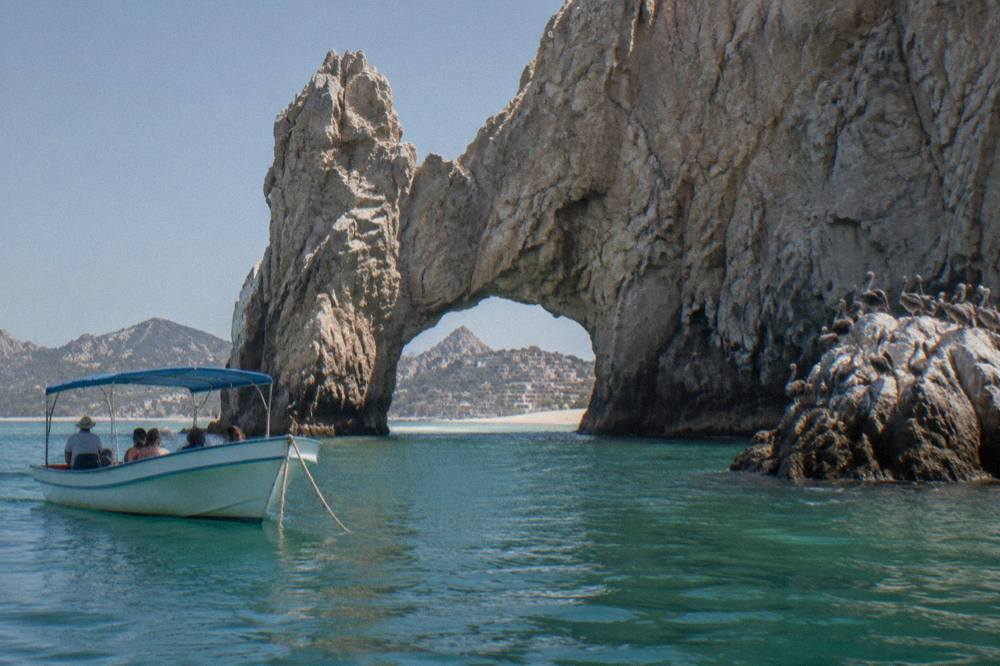 A boat passing close to tall granite rock formations at the tip of a peninsula with calm water below
