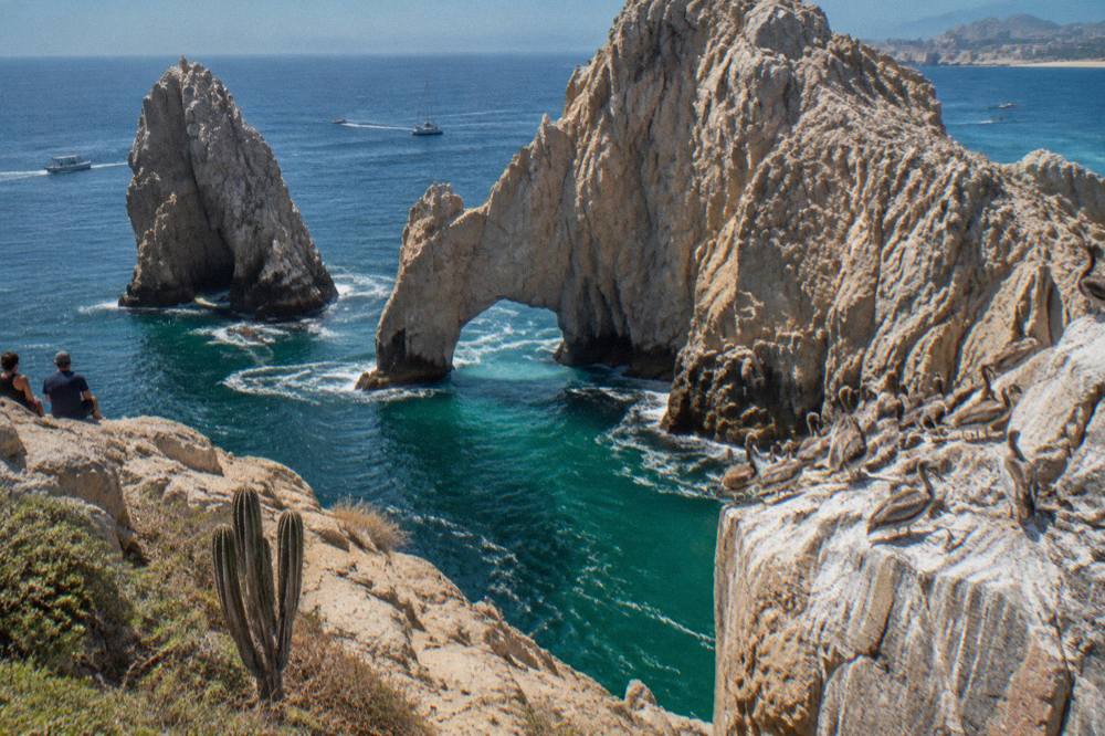 Granite rock arch at the tip of a peninsula with calm blue water passing beneath it