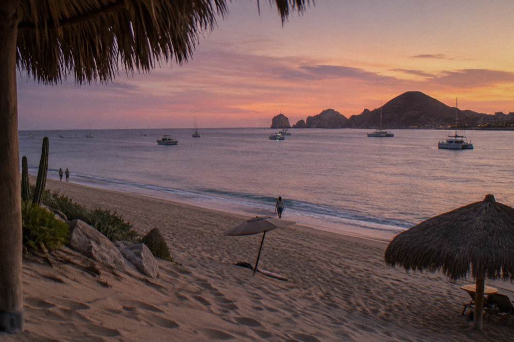 Wide sandy beach with calm water and boats at anchor in the distance at dusk