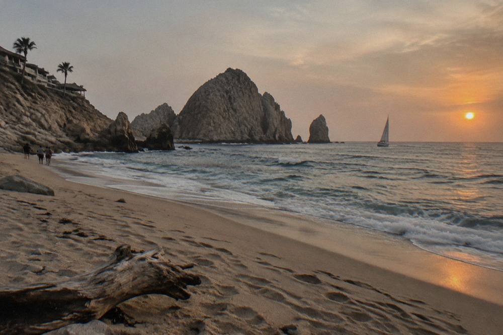 Sun sinking toward the Pacific horizon behind a sailboat heeling gently offshore