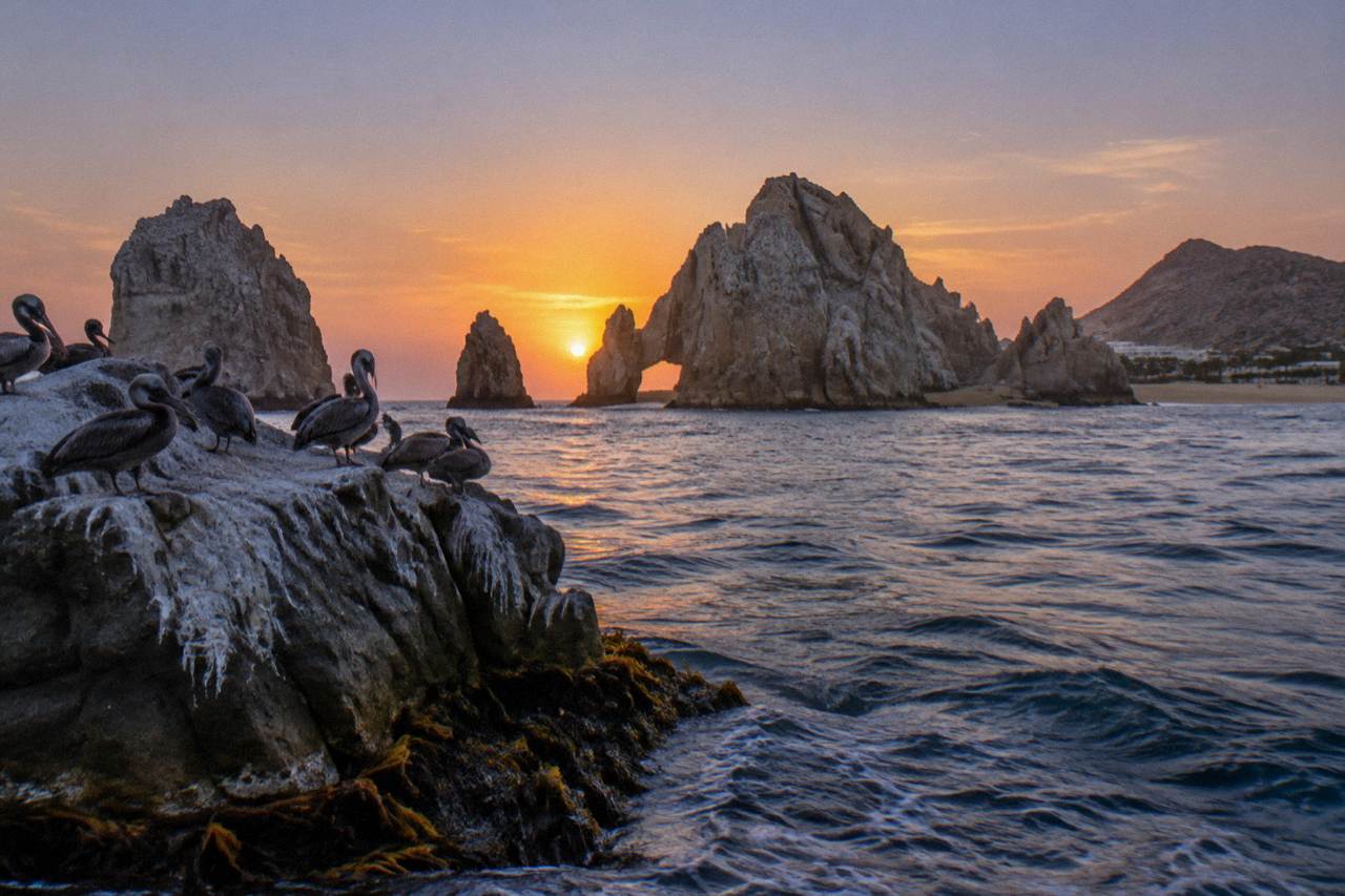 Sunset sky in orange and violet tones over rock formations at the end of the Cabo San Lucas coastline