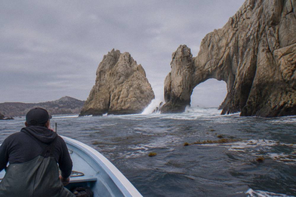 Small boat passing close to a granite arch at the tip of a rocky headland