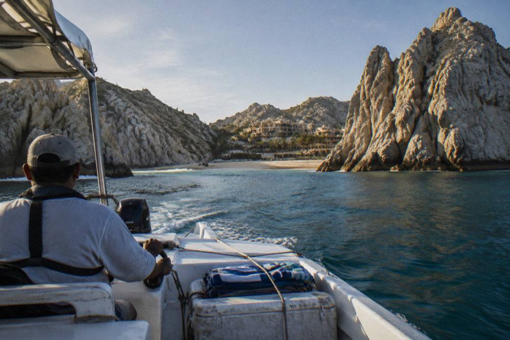 Small water taxi boat approaching a granite cove at Land's End in Cabo San Lucas