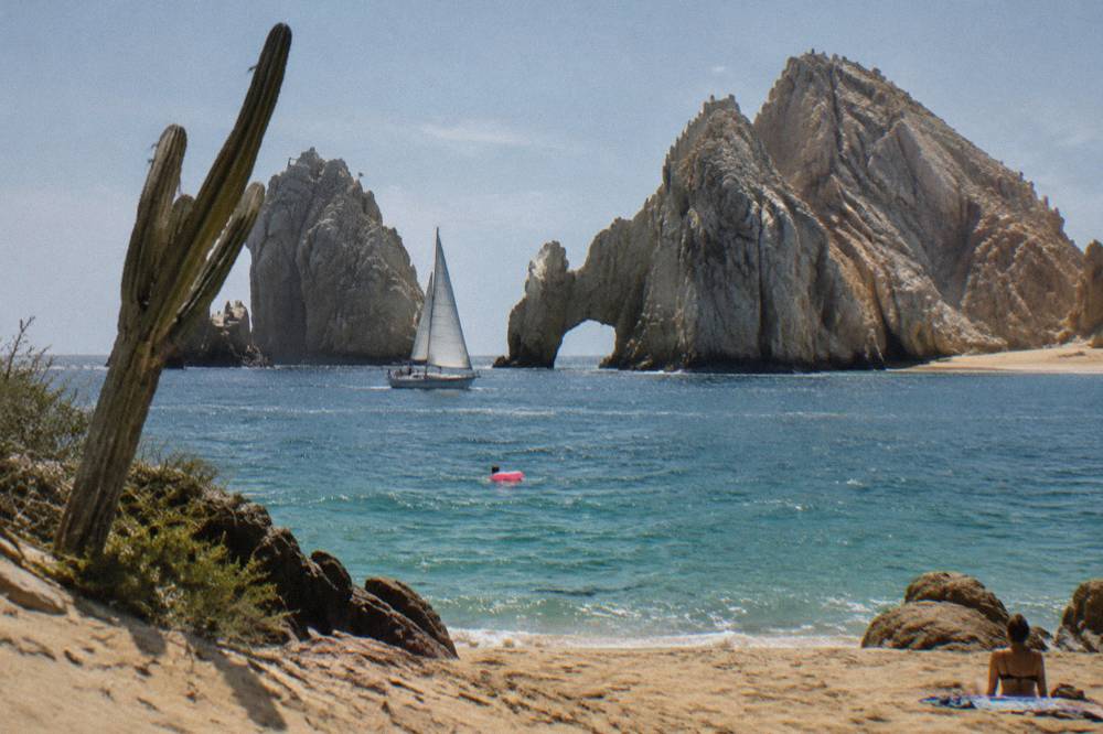 Sailboat passing the rock arch at Land's End under warm late afternoon light