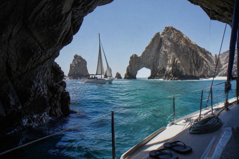 A sailboat passing the rock arch at Land's End under a clear sky