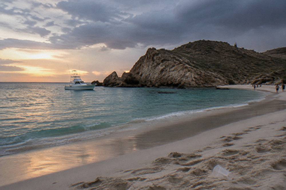 An anchored boat in clear turquoise water near a rocky point at dusk