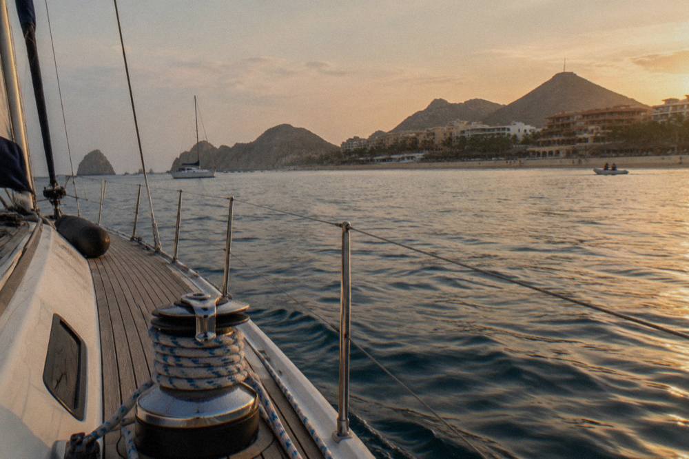 Sailboat under golden light on calm water near the Cabo San Lucas coastline