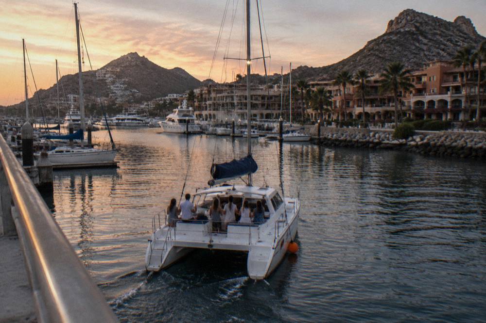 Catamaran with passengers on deck leaving the Cabo San Lucas marina at dusk
