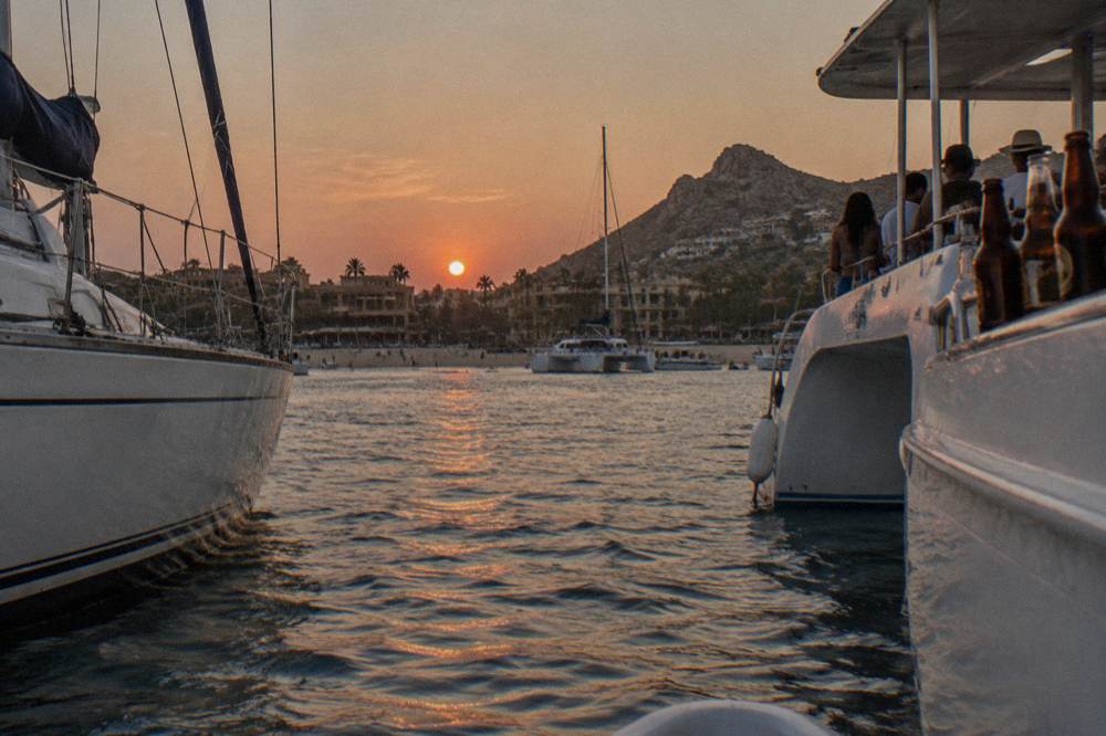 Two boats on the water near Cabo San Lucas, a sailing yacht and a larger party vessel, at golden hour