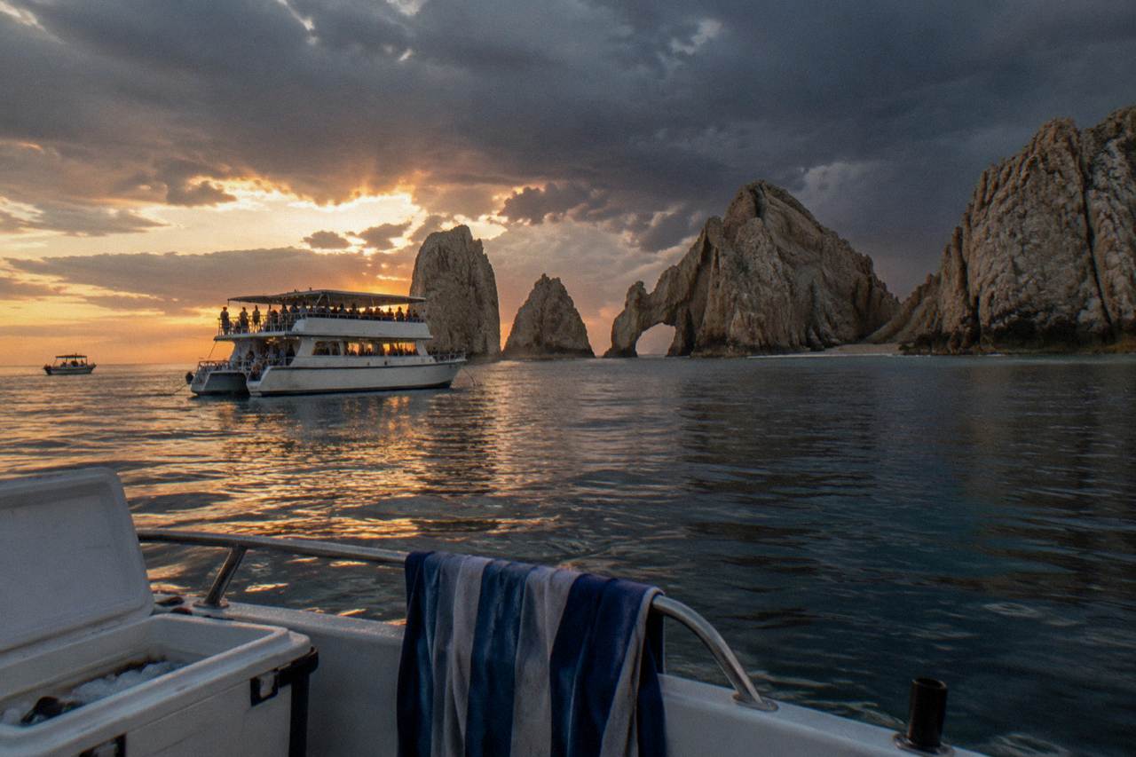 Party cruise boat on open water near Cabo San Lucas at sunset with calm sea and distant rocks