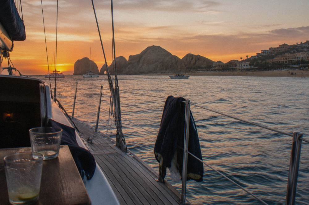 Deck of a sailing yacht at sunset with railing, rigging lines and warm light over the water