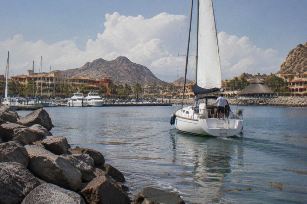 Sailboat heading out of the Cabo San Lucas marina under a partly cloudy sky