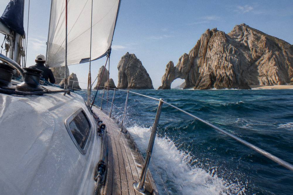Sailing yacht under way near the Arch at Cabo San Lucas with white sails raised
