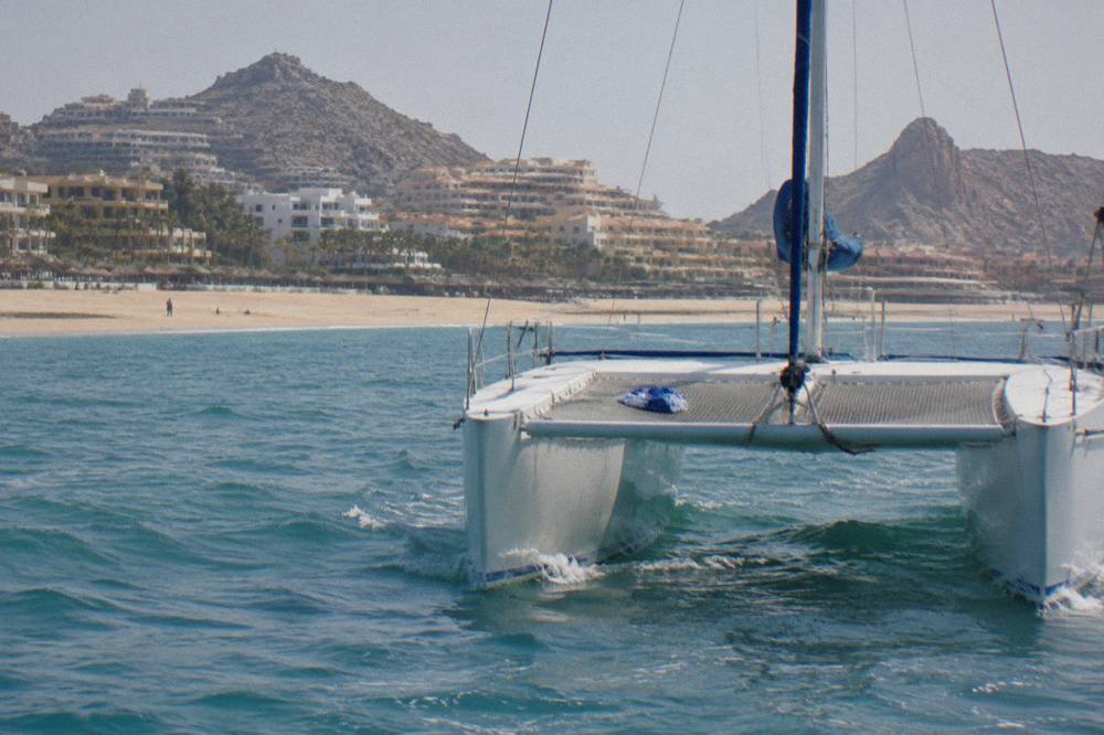 Two catamaran hulls cutting through calm water with a wide deck between them