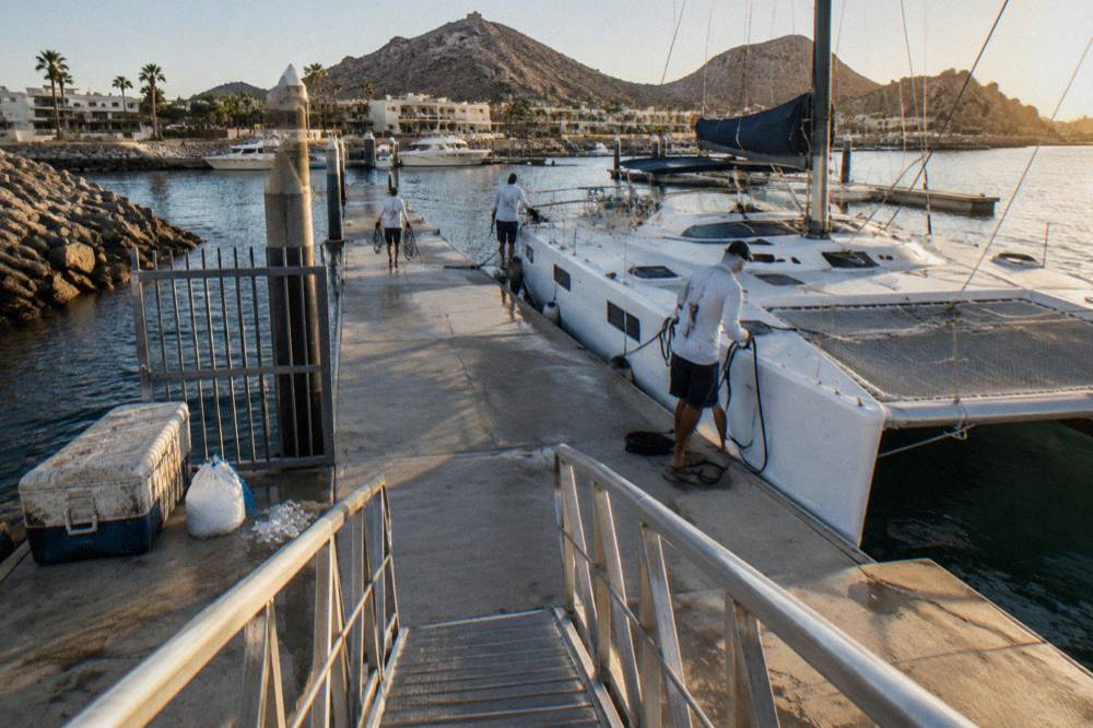 A catamaran moored at a marina dock with crew preparing the deck before departure