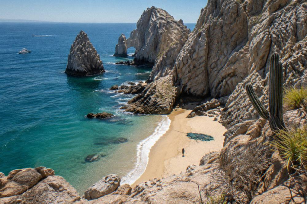 Towering granite cliffs at Land's End dropping into blue water with a narrow sand strip below
