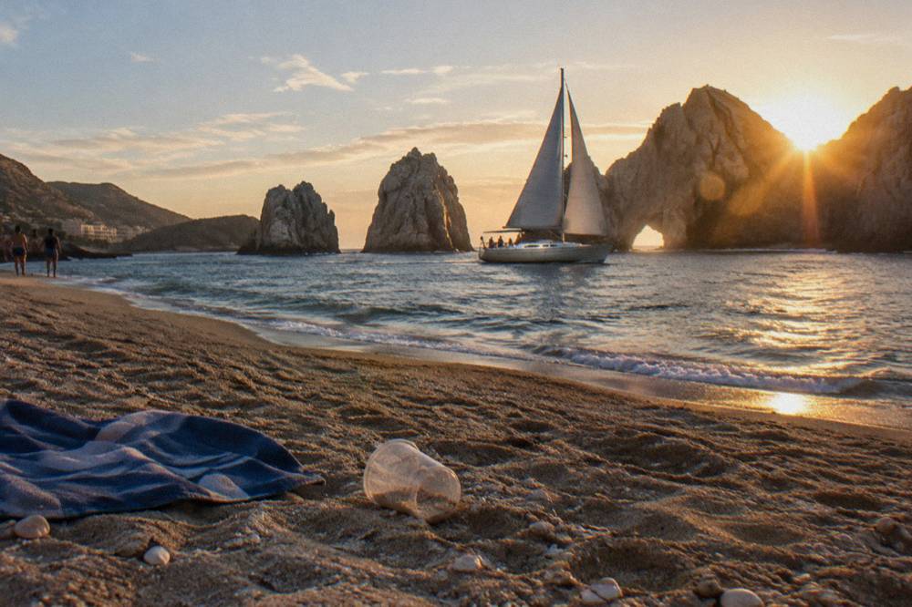 A sailing yacht under way near Land's End with warm evening light on the rocks