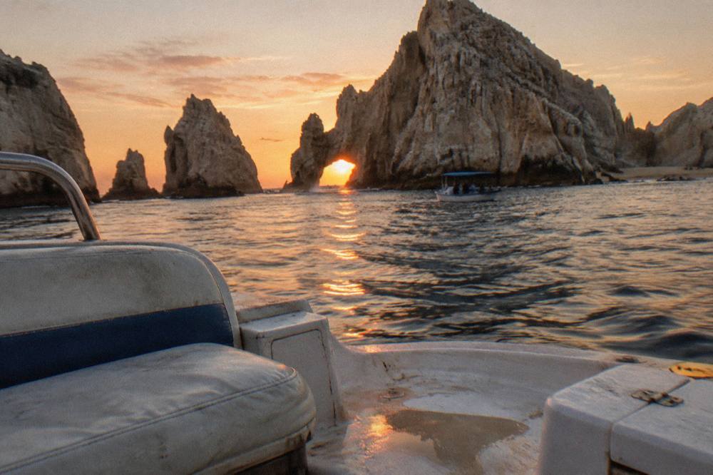 Warm sunset light on the arch at Land's End seen from the water with an orange sky