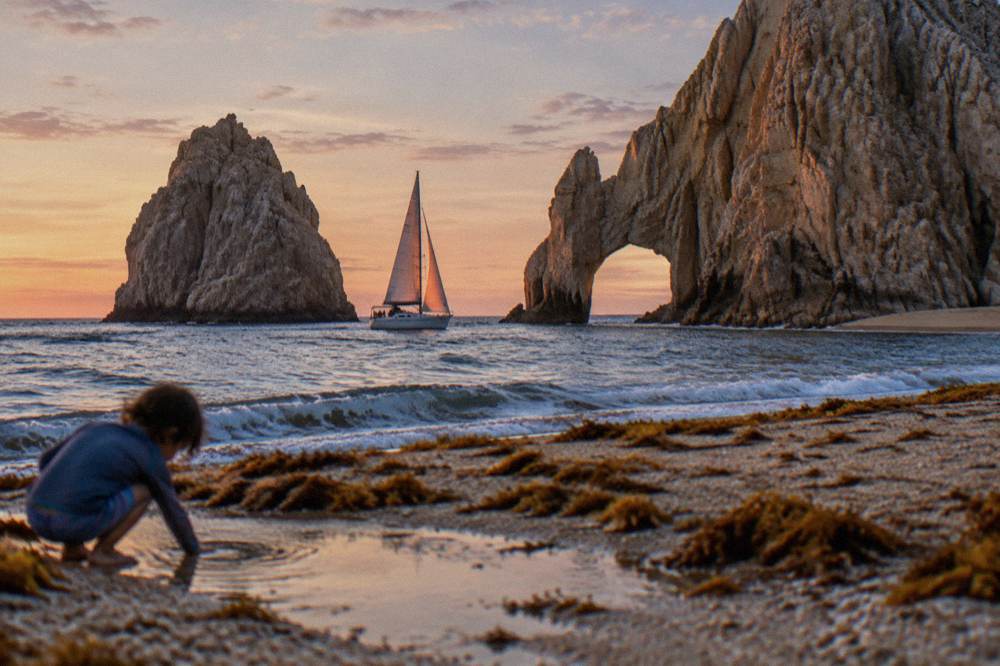 Sailboat passing close to the rock arch at Land's End in warm evening light