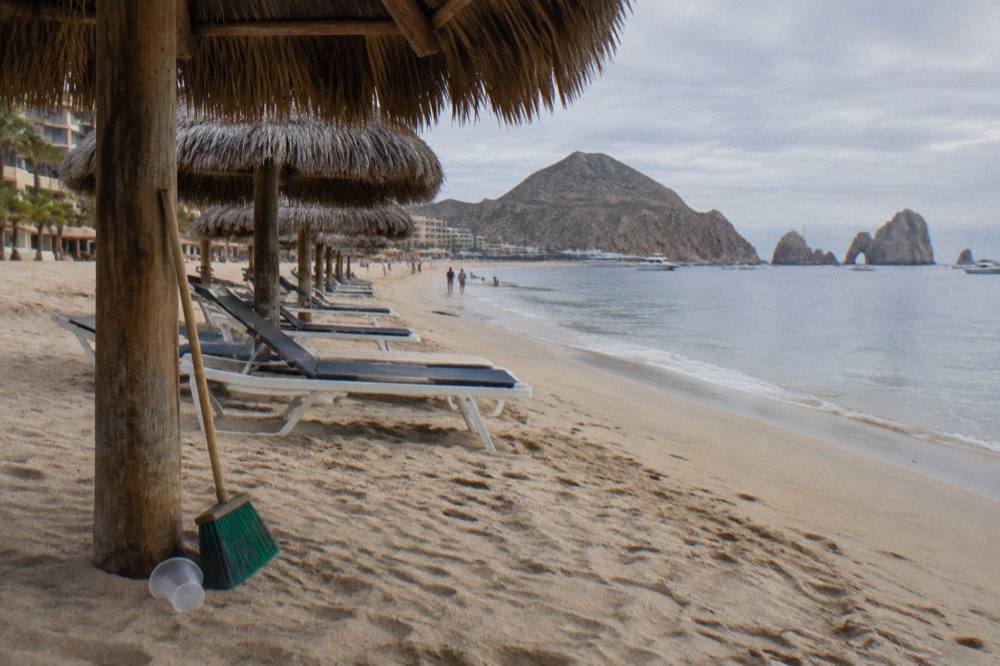 Palm-thatched umbrellas and lounge chairs on a wide beach beside calm shallow water