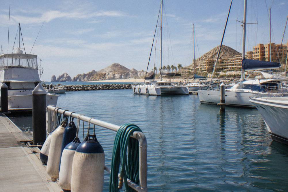 Yachts and catamarans moored in a marina basin with a sandy beach and rocky point beyond