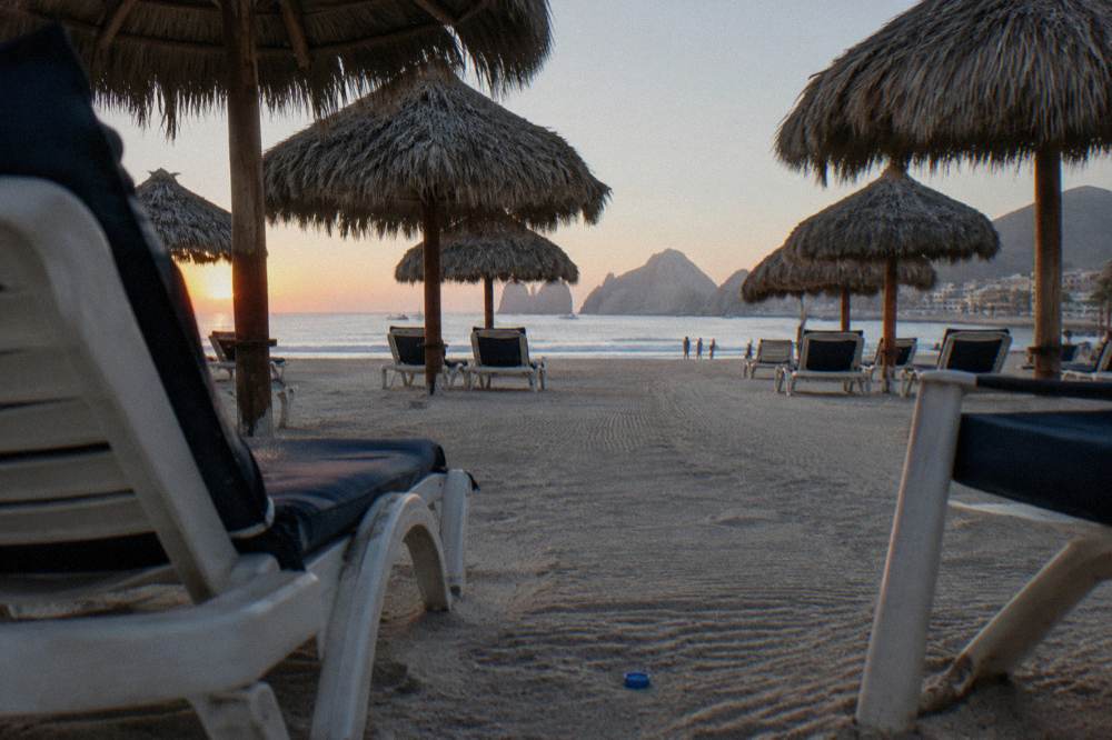 Rows of empty lounge chairs and thatched palapas on sand in early morning light