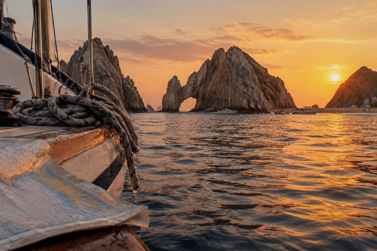 A sailboat on calm water near rock formations at dusk, warm orange sky