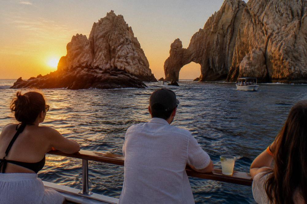 Dinner cruise passengers on deck looking toward the Arch rock formation at sunset