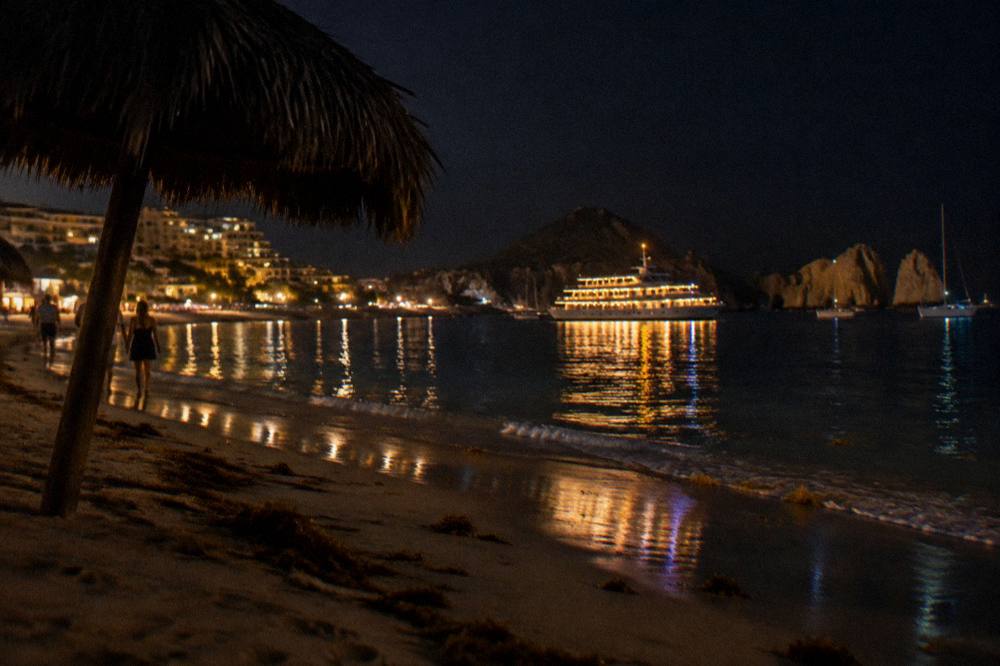 A yacht with dinner lights aboard cruising the Cabo San Lucas bay after sunset