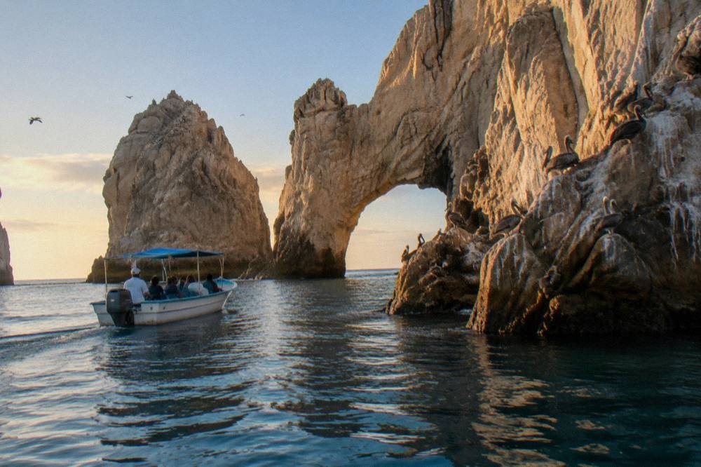 Rocks at Land's End and the Arch lit by warm low sun over calm water