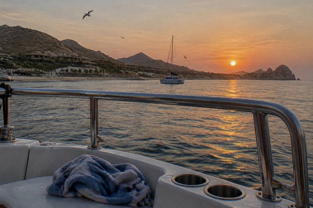 Sun sinking into the Pacific horizon behind a boat rail in Cabo San Lucas