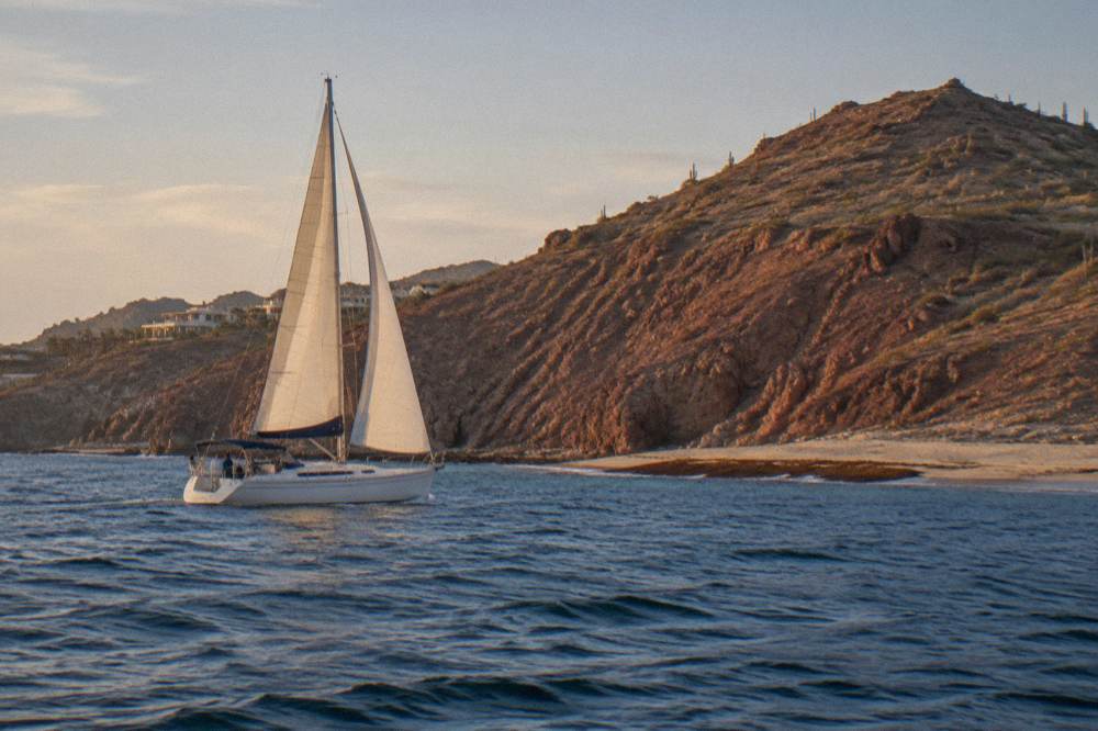 Sailboat under full sail cruising past rocky headland in golden evening light