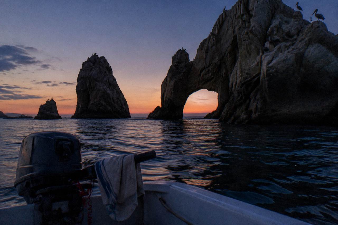Rock arch formation at Land's End rising above calm water at dusk