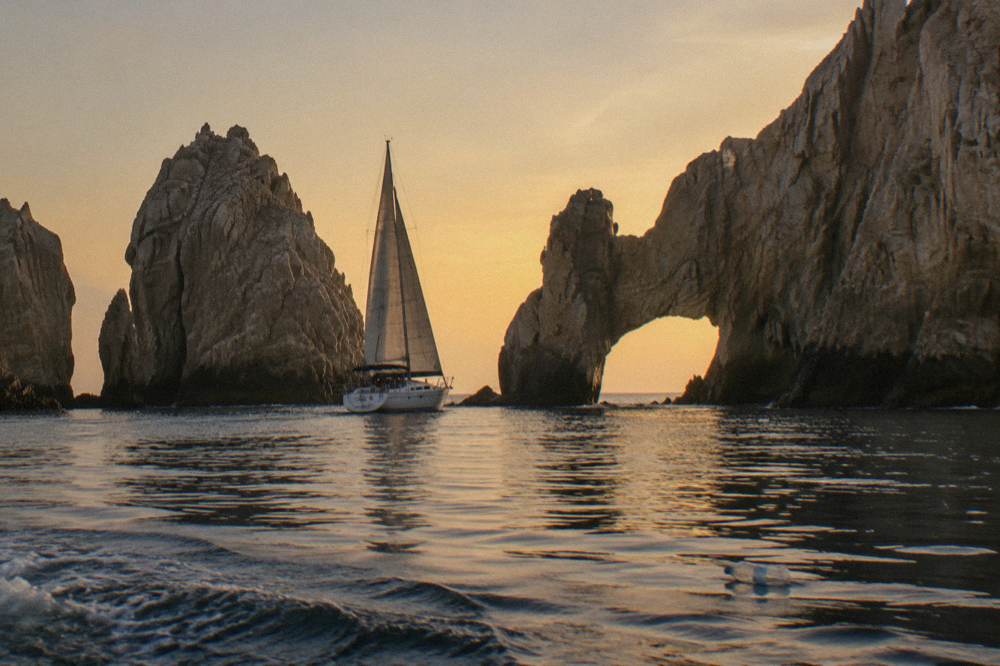 Sailboat passing a stone arch formation at golden hour on calm water