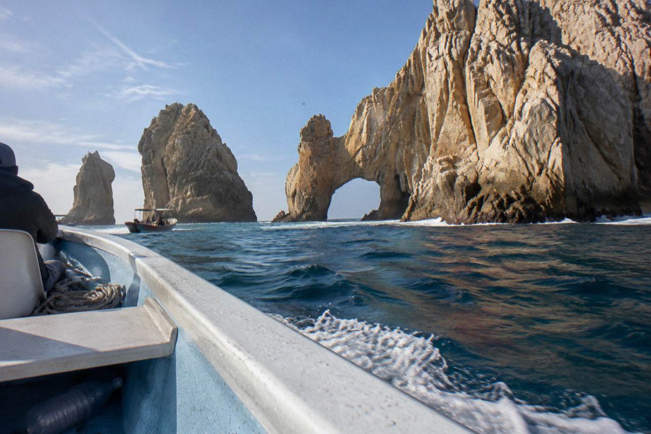 Small open boat approaching golden rock cliffs at the entrance to Cabo San Lucas bay