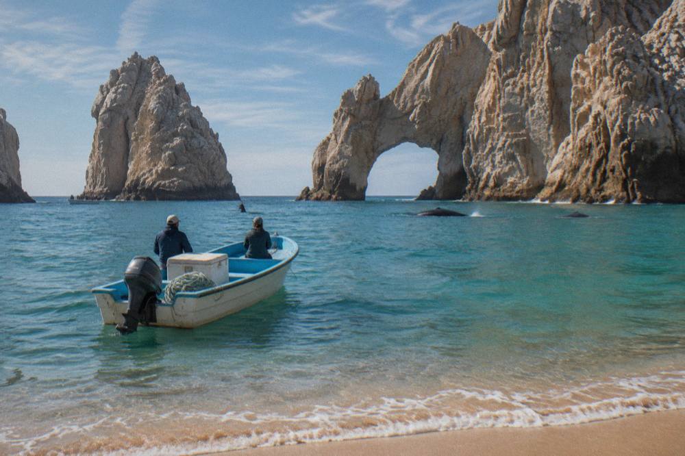 A small tour boat on calm blue water near the stone arch at the tip of the Baja peninsula