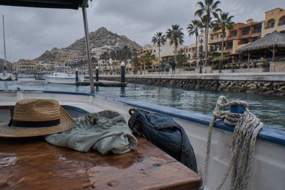 Light jackets and a sun hat laid out on a boat bench beside a small day pack
