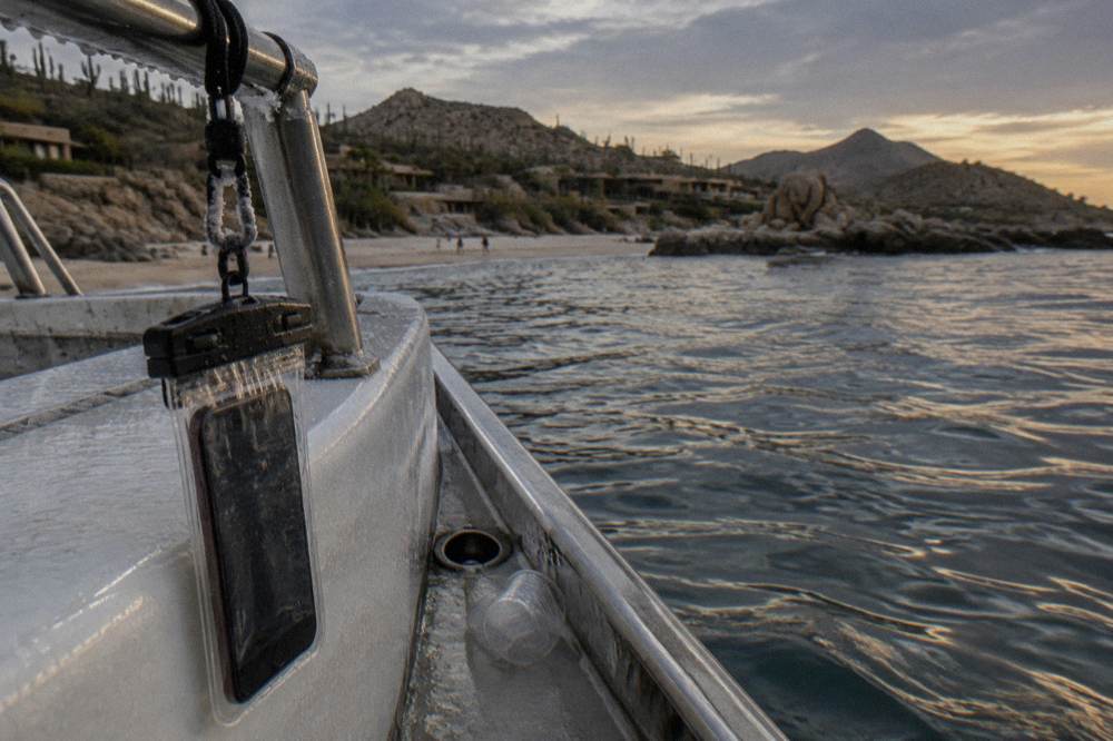 A smartphone in a clear waterproof pouch hanging from a lanyard on a boat railing at dusk